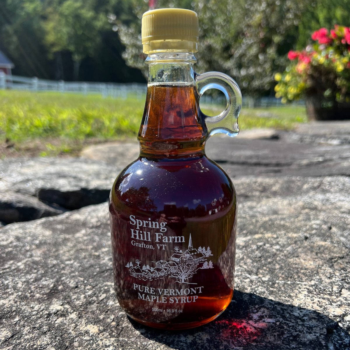 glass bottle of maple syrup sitting on grey stone - spring hill farm grafton, vermont