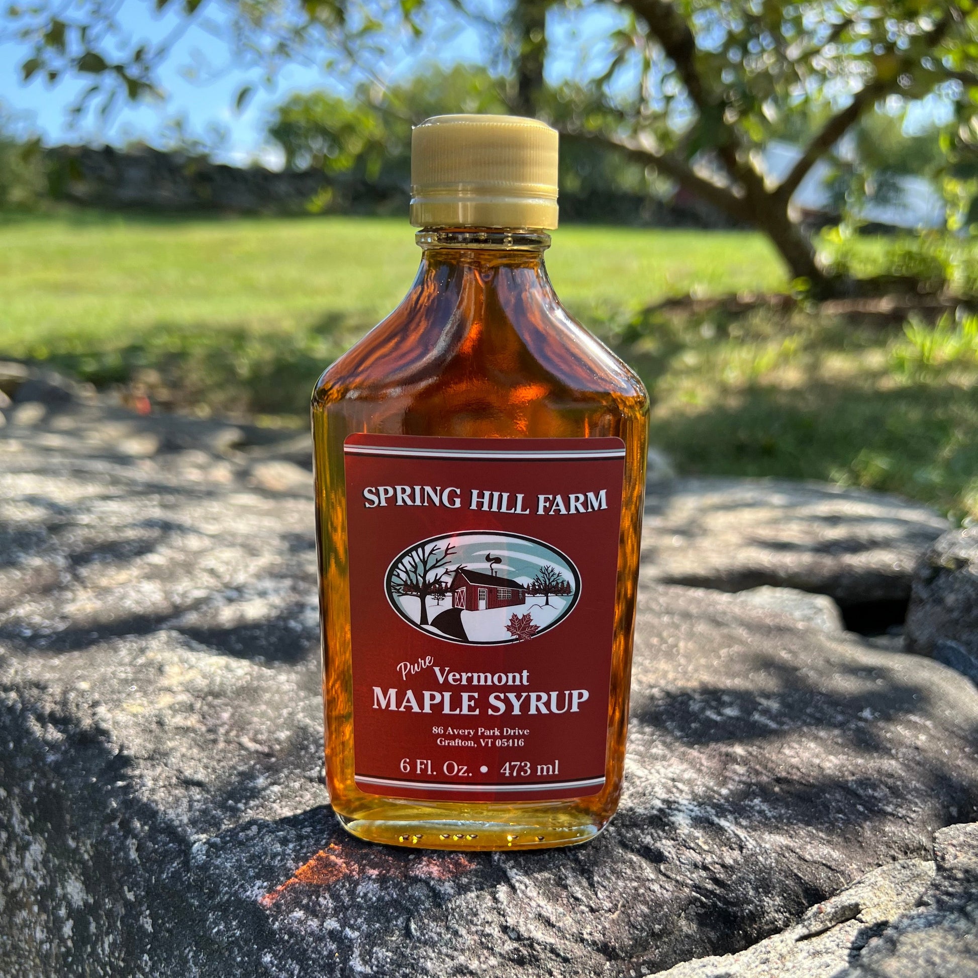 glass flask bottle of pure vermont maple syrup with Spring Hill label sitting on a Vermont stone wall