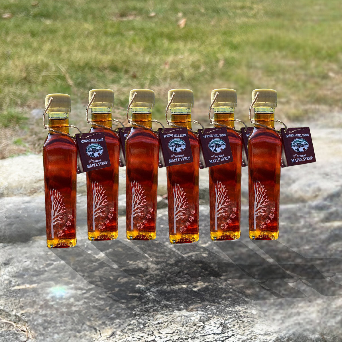 6 pack of engraved glass maple syrup bottles on a stone wall - spring hill farm maple syrup