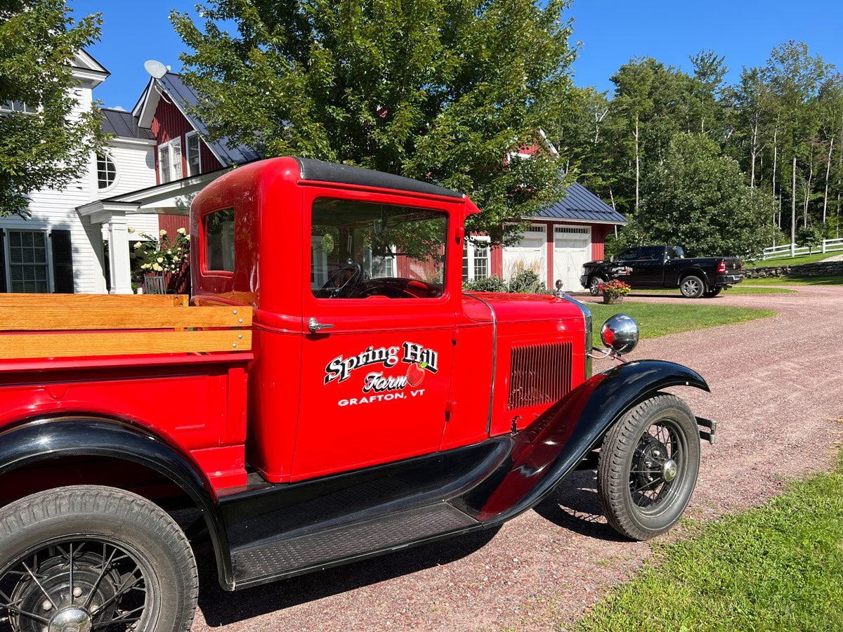Red vintage truck with spring hill farm grafton vermont logo on the door in front of traditional vermont farmhouse