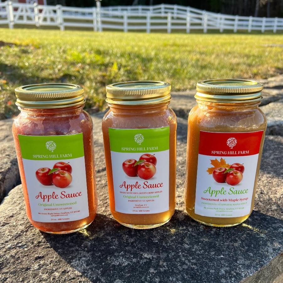 gourmet applesauce collection. three mason jars of applesauce sitting on a stonewall in from of a field and white fence.